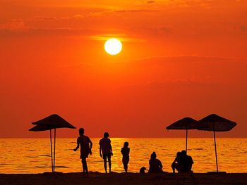 Silhouette people on beach against orange sky