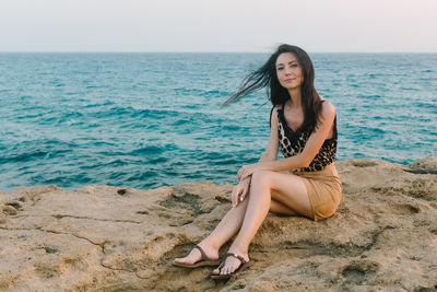 Portrait of young woman sitting on shore against sea