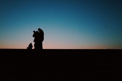 Silhouette man photographing woman standing against clear sky during sunset