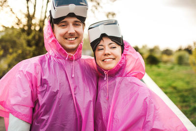 Happy young couple wearing raincoat and virtual reality simulator at park