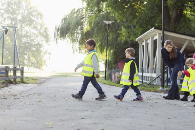 Children in protective jacket with teacher walking on footpath