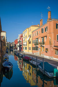 Boats moored in city against clear blue sky