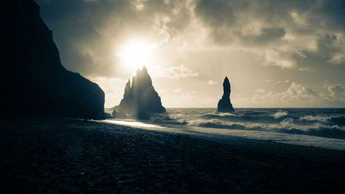 Silhouette rocks on beach against sky during sunset