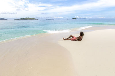 Woman relaxing on beach against sky