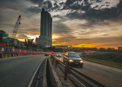 Cars on street in city against sky during sunset