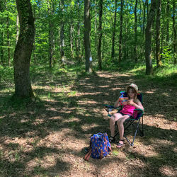 Girl sitting on chair against trees at forest