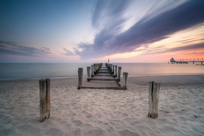 Wooden posts on beach against sky during sunset