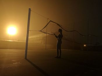 Full length of woman standing by volleyball net at night