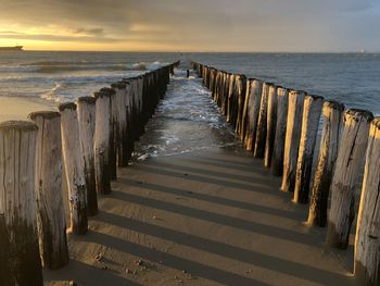 Wooden posts on beach against sky during sunset