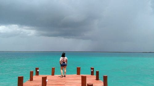 Woman standing on pier over sea against sky