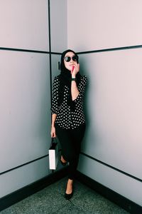 Full length of woman wearing sunglasses while standing against wall