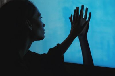 Close-up of woman trying to touch person hand against blue sky