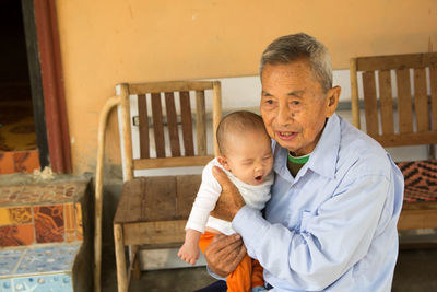 Senior man holding grandson against house 