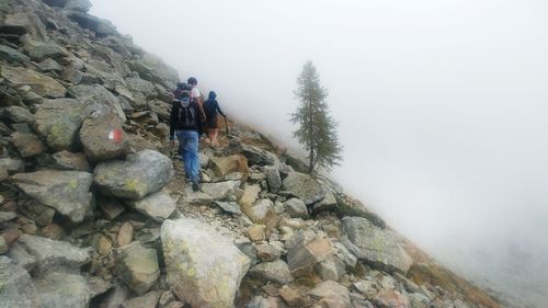 Rear view of man standing on rock against sky during foggy weather