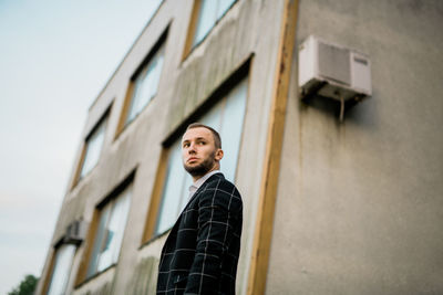 Low angle view of young man looking away while standing against building