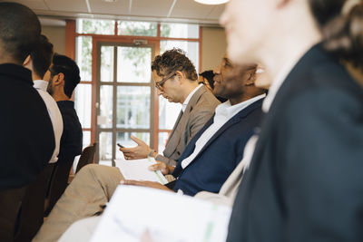 Male entrepreneur using phone while sitting with colleagues in office workshop