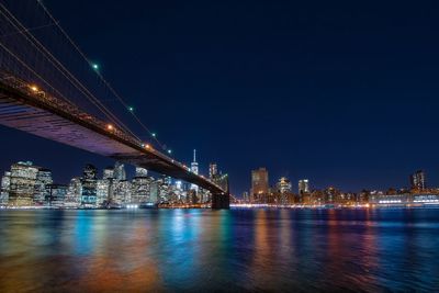 Illuminated brooklyn bridge over east river against sky at night