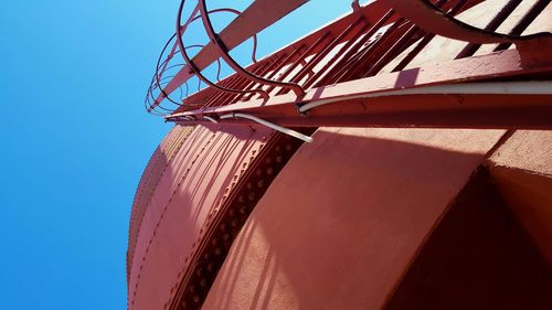 Low angle view of ladder on storage tank against clear blue sky