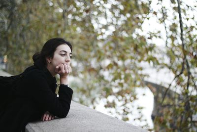 Thoughtful young woman looking away while leaning on retaining wall