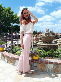 Portrait of smiling young woman standing against fountain during sunny day