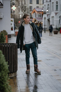 A full-length photograph of a young guy walking in a cold city, wearing a winter jacket and warm 