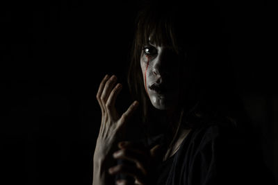 Portrait of young woman with halloween make-up against black background