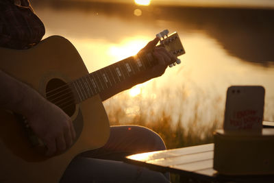 Midsection of man playing guitar during sunset