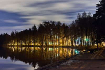Silhouette trees by lake in forest against sky
