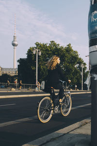 Woman riding bicycle on road in city against sky