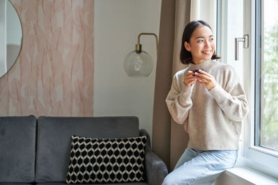 Portrait of young woman using mobile phone while sitting on chair at home