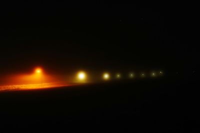 Illuminated street lights against sky at night