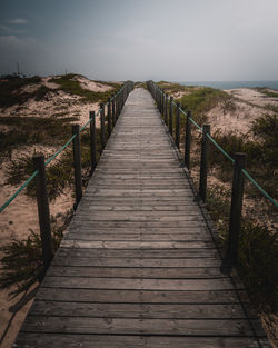 Empty wooden boardwalk at beach against sky