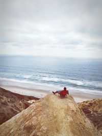 Man sitting on rock formation against sea at beach