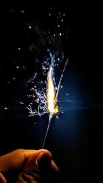 Cropped hand of person holding illuminated sparkler at night