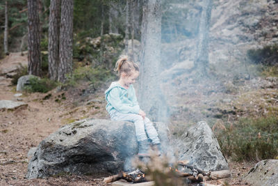 Young girl sitting by a campfire warming up in the forest in sweden