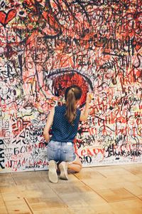 Rear view of woman standing against graffiti wall