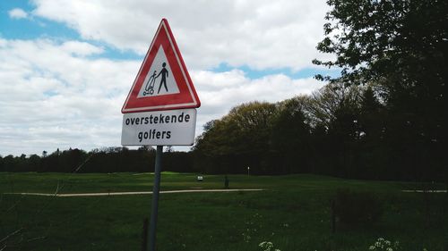 Road sign by trees against sky