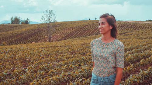 Young woman standing on field against sky