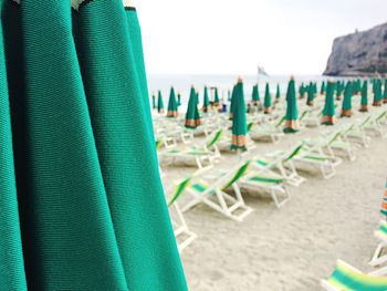 Closed green parasols by empty deck chairs at sandy beach