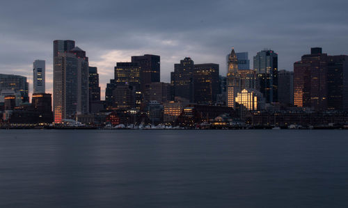 Illuminated buildings by sea against sky at dusk