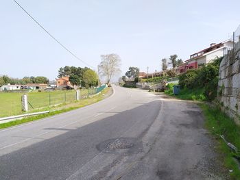 Road by buildings in city against clear sky