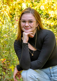 Pretty young lady sits outdoor in a golden and green woods, and poses for a senior portrait