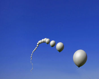 Low angle view of gray balloons against clear blue sky on sunny day