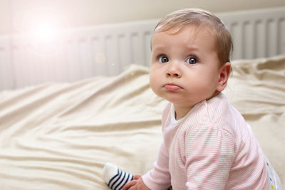 Close-up portrait of cute baby girl sitting on bed at home