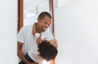 Father carrying son while standing against wall