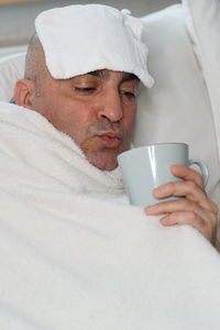 Man suffering from headache having coffee on bed at home