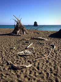 Face made up of driftwood on rippled sand at beach against clear blue sky