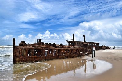 Abandoned wooden post on beach against sky