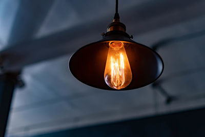 Low angle view of illuminated light bulb hanging from ceiling