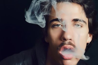 Close-up portrait of man smoking against black background